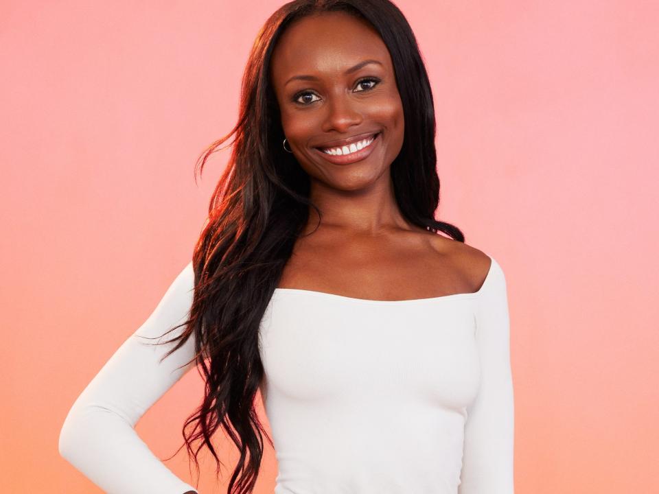 Kyra poses for photos in a white shirt and brown skirt.