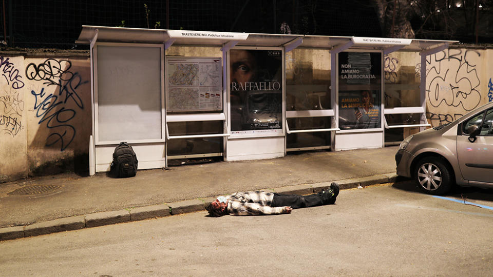 A man wearing a protective mask is on the ground unconscious near a bus stop before being helped by medical personnel as the spread of the coronavirus persists in Italy. Source: Getty Images