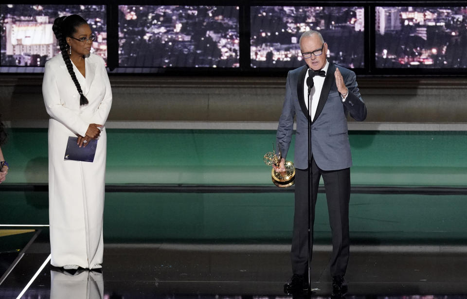 Michael Keaton, right, accepts the Emmy for outstanding lead actor in a limited or anthology series or movie for "Dopesick" at the 74th Primetime Emmy Awards on Monday, Sept. 12, 2022, at the Microsoft Theater in Los Angeles. Oprah Winfrey looks on from stage left. (AP Photo/Mark Terrill)