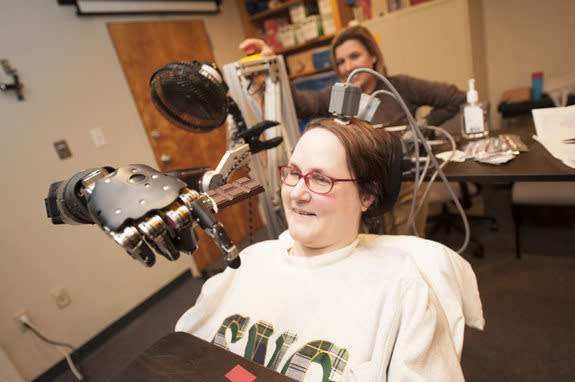 Jan Scheuermann, who has quadriplegia, brings a chocolate bar to her mouth using a robot arm she is guiding with her thoughts. Research assistant Elke Brown, M.D., watches in the background.