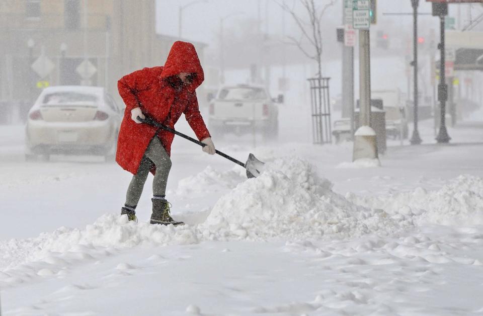 Eve Kostelecky clears snow from the front of her business on Main Street in downtown Mandan, N.D., in blizzard conditions early Wednesday, April 5, 2023. The storm that left nearly 4 inches of snow in the Bismarck Mandan area that is approaching a record amount of snowfall. (Tom Stromme/The Bismarck Tribune via AP)