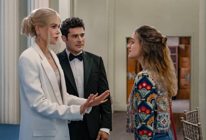 Nicole Kidman, Zac Efron in a black tuxedo, and Joey King in a patterned jacket have a conversation indoors in a scene from A Family Affair