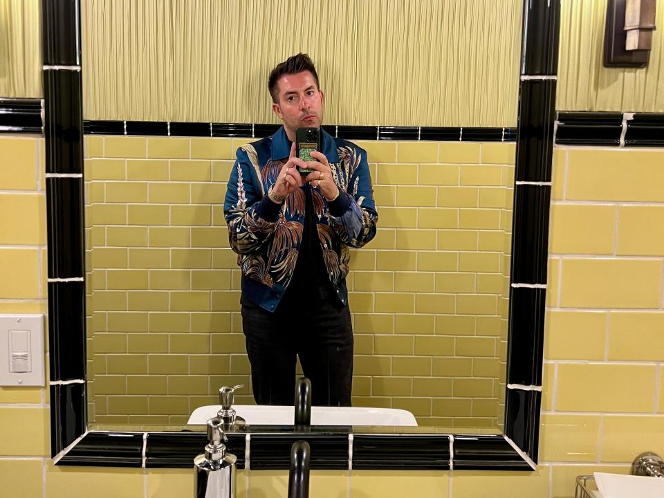 A man taking a selfie in a bathroom mirror with yellow tiled walls.