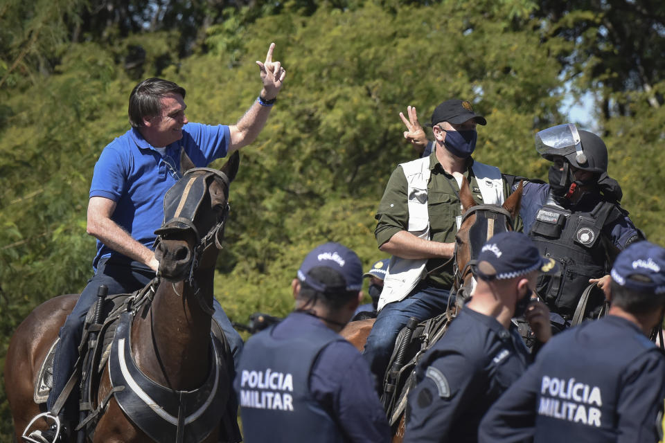 Brazil's President Jair Bolsonaro rides a horse greeting supporters outside the presidential palace in Brasilia, Brazil, Sunday, May 31, 2020. Bolsonaro mounted a horse from police that were guarding supporters of his government gathered outside the Planalto Palace. (AP Photo/Andre Borges)