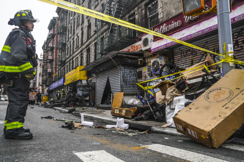 A firefighter stands near debris in the aftermath of a fire in Chinatown which authorities say started at an e-bike shop and spread to upper-floor apartments, killing four people and injuring several others, Tuesday June 20, 2023, in New York. (AP Photo/Bebeto Matthews)