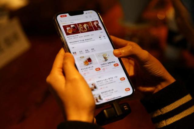 A journalist checks the Starbucks menu on the Meituan app on her phone during a media event of Starbucks launching a partnership with Meituan, in Beijing