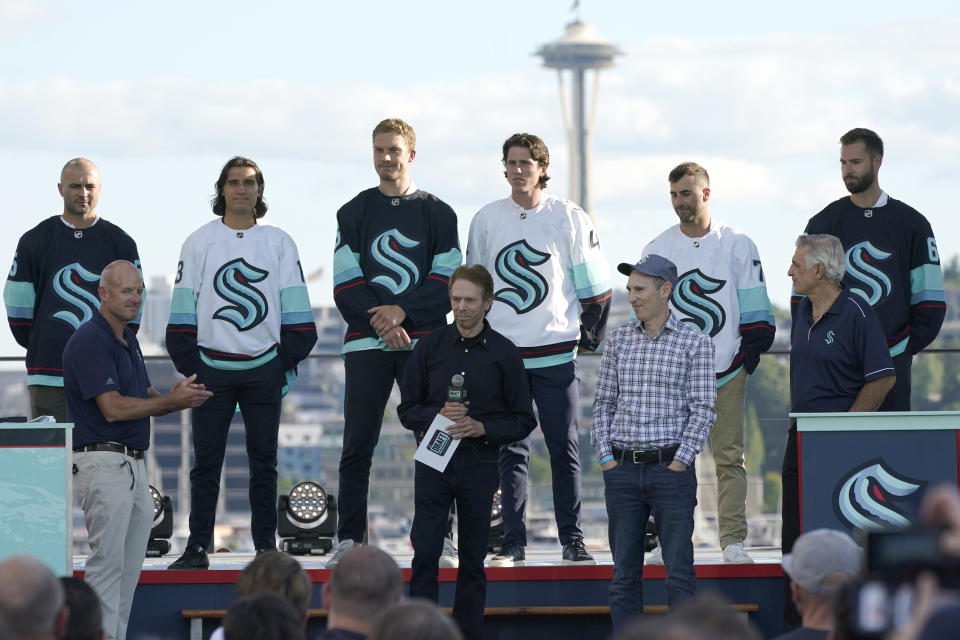FILE - Seattle Kraken owners Jerry Bruckheimer, front center, is joined by owners David Wright, front left, and Andy Jassy, front second from right, with Kraken general manager Ron Francis, front right, and new Seattle Kraken NHL hockey players, back row from left, Mark Giordano, Brandon Tanev, Jamie Oleksiak, Hadyn Fluery, Jordan Eberle and Chris Dreidger, Wednesday, July 21, 2021, after being introduced during the Kraken's expansion draft event in Seattle. With Hollywood filmmaker Jerry Bruckheimer as part of the ownership group, the Seattle Kraken were always going to have a big cinematic element to any video production the team produced. (AP Photo/Ted S. Warren, File)