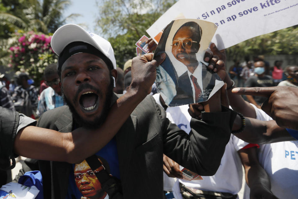 Supporters of former Haitian President Jean-Bertrand Aristide celebrate as they wait at the airport for his expected arrival from Cuba, where he underwent medical treatment, in Port-au-Prince, Haiti, Friday, July 16, 2021. Aristide's return adds a potentially volatile element to an already tense situation in a country facing a power vacuum following the July 7 assassination of President Jovenel Moïse. (AP Photo/Fernando Llano)