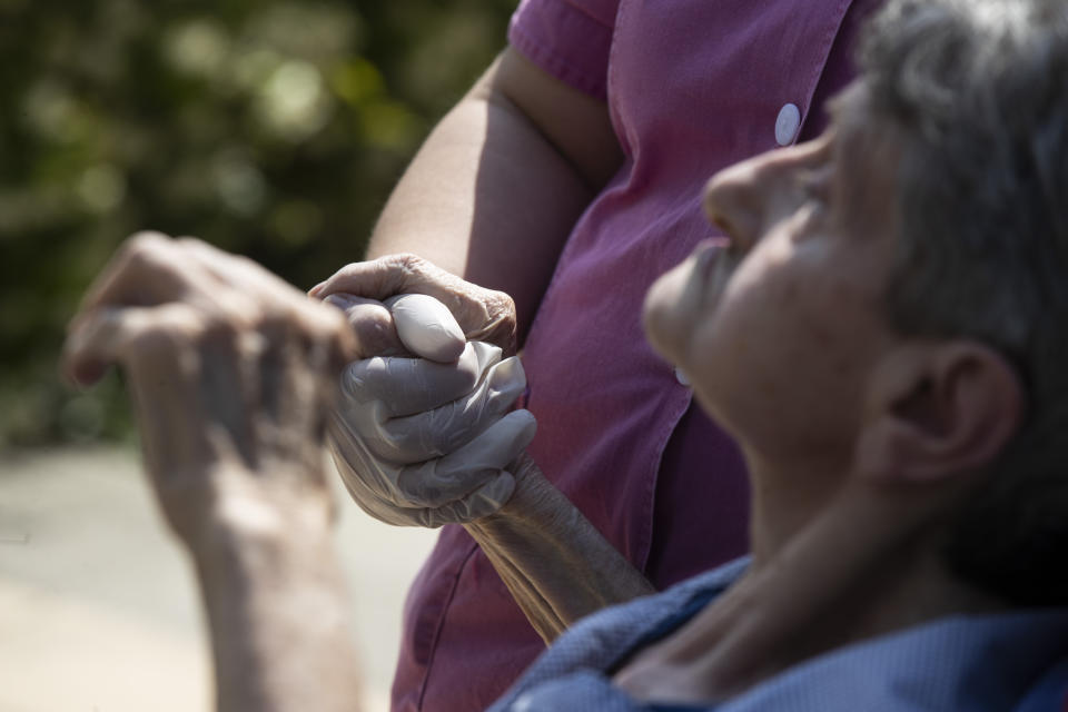 Anna Maria Alborghetti sits in a wheelchair as carer Melania Cavalieri holds her hand during a visit by her family at the Martino Zanchi Foundation nursing home in Alzano Lombardo, Italy, Friday, May 29, 2020. (AP Photo/Luca Bruno)