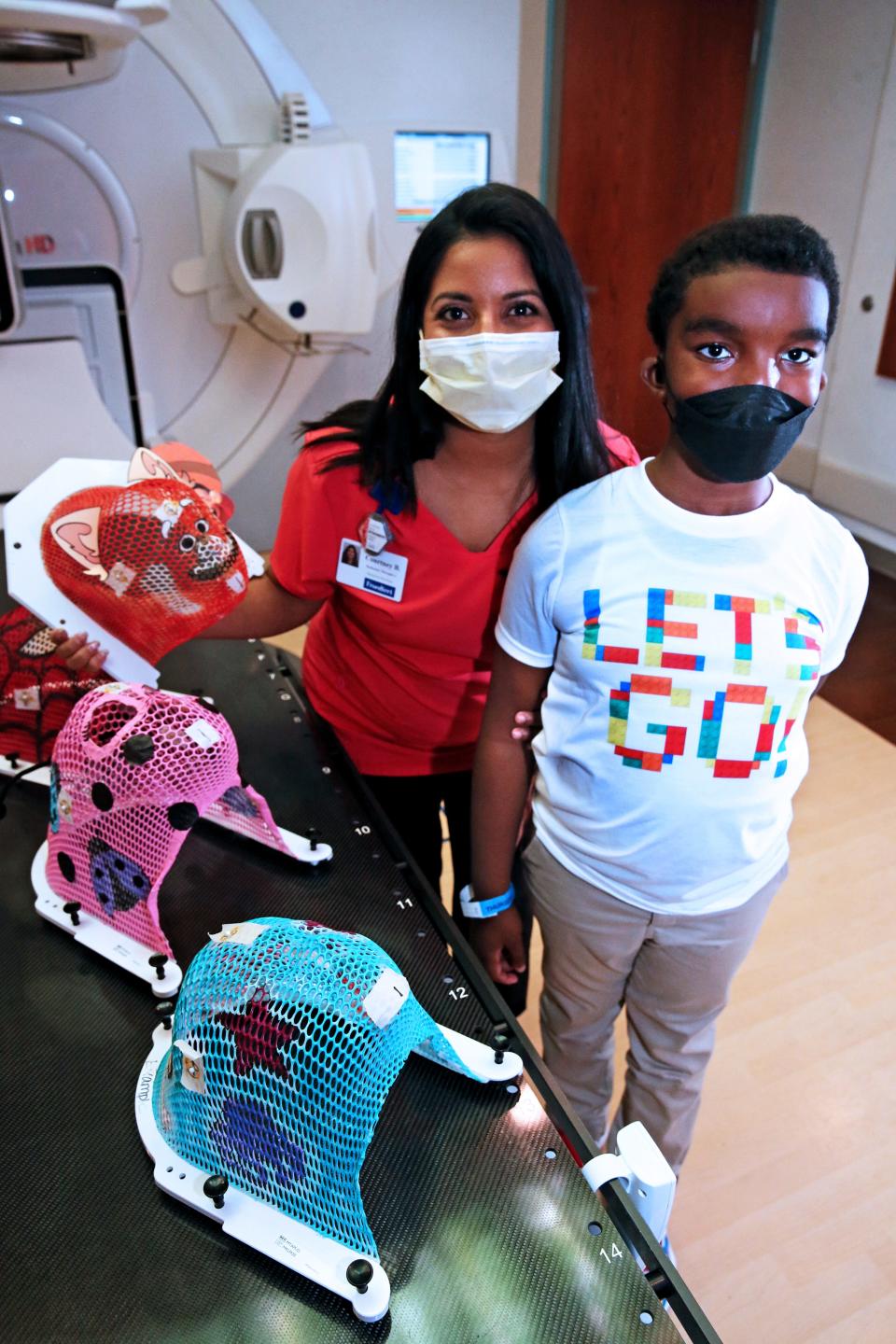 Radiation therapist Courtney Shanmugabaskaran, left and Caidence Carnes, 8,right, are photographed in one of the radiation rooms that Carnes received treatment in 2019.  Shanmugabaskaran holds and displays some the masks she designed for pediatric patients receiving radiation treatment at the Cancer Center at Children’s Wisconsin; Froedtert & MCW. Carnes received treatment in 2019 and Shanmugabaskaran painted a mask for him in the design of a Power Ranger.