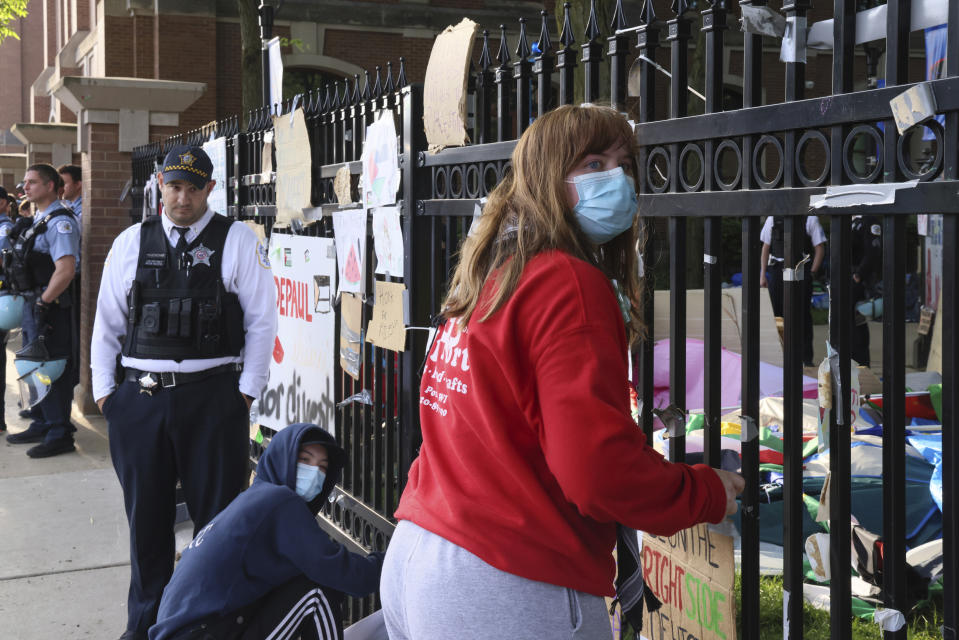 A Chicago police officer looks on as protesters remove signs from a fence around DePaul University's campus quad in Chicago, Thursday, May 16, 2024. Police dismantled a pro-Palestinian encampment at the university. It was taken down in the early morning, hours after the school's president told students to leave the area or face arrest. Students at many college campuses this spring set up similar encampments, calling for their schools to cut ties with Israel and businesses that support it, to protest Israel's actions in the war with Hamas. (AP Photo/Teresa Crawford)