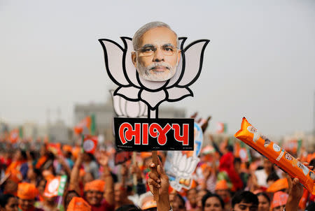 A supporter holds up a cut-out of a lotus, the election symbol of India's ruling Bharatiya Janata party (BJP), with an image of Prime Minister Narendra Modi during a campaign meeting addressed by Modi ahead of Gujarat state assembly election in Kalol on the outskirts of Ahmedabad, December 8, 2017. REUTERS/Amit Dave/Files