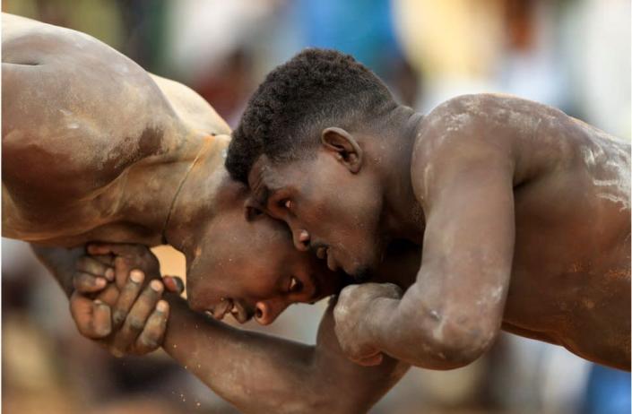 Two men tacking part in wrestling. They are shirtless and have what looks like chalk on their bodies.