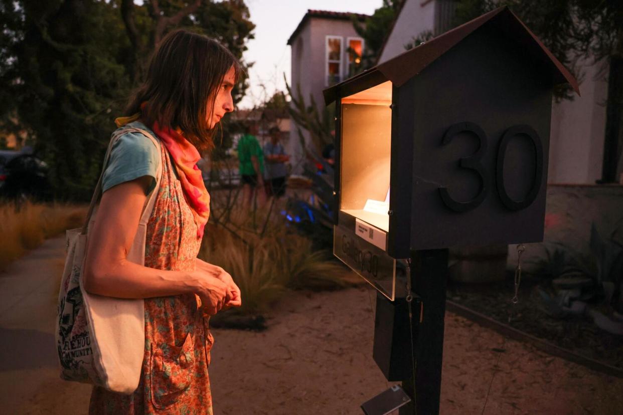 A woman peeks inside a lighted micro art gallery at dusk.