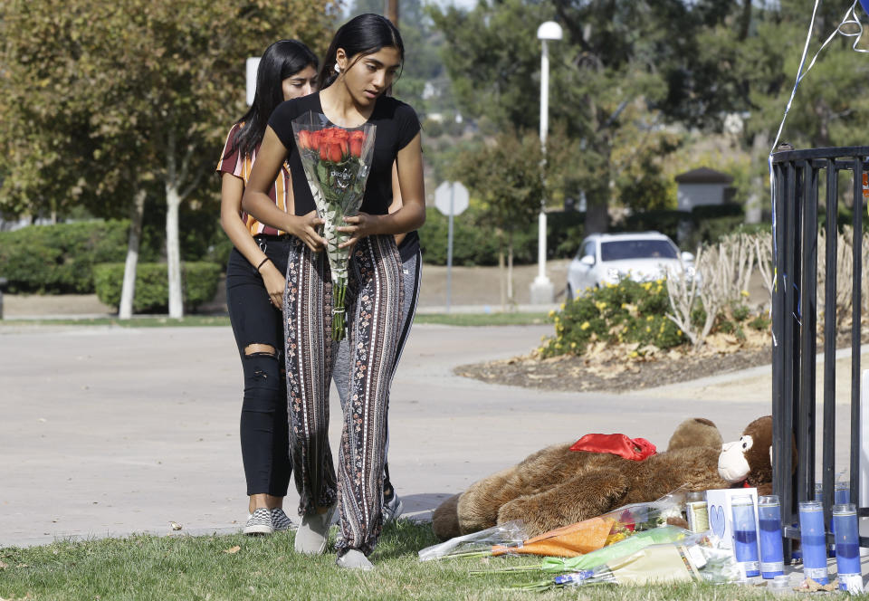 Saugus High School students Liliana, 15, right and her sister Alexandra, 16 bring a bouquet of roses for the Saugus High School victims at the Central Park in Santa Clarita, Calif., Friday, Nov. 15, 2019. A homicide official says that investigators did not find a diary, manifesto or note belonging to the boy who killed two people outside his Southern California high school on his 16th birthday. Officials held a press conference Friday outside of the police station Santa Clarita. No motive or rationale has been established yet in the Thursday morning shooting at Saugus High School in the Los Angeles suburb of Santa Clarita. (AP Photo/Damian Dovarganes)