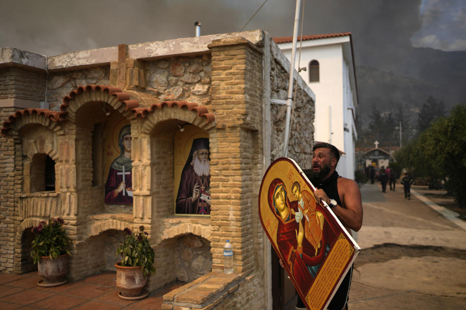 A man carries a saint Mary with Jesus icon to save it from a wildfire at Agia Paraskevi Christian Orthodox monastery in Acharnes a suburb of northern Athens, Greece, Wednesday, Aug. 23, 2023. Water-dropping planes from several European countries joined hundreds of firefighters Wednesday battling wildfires raging for days across Greece that have left 20 people dead, while major blazes were also burning in Spain's Tenerife and in northwestern Turkey near the Greek border. (AP Photo/Thanassis Stavrakis)