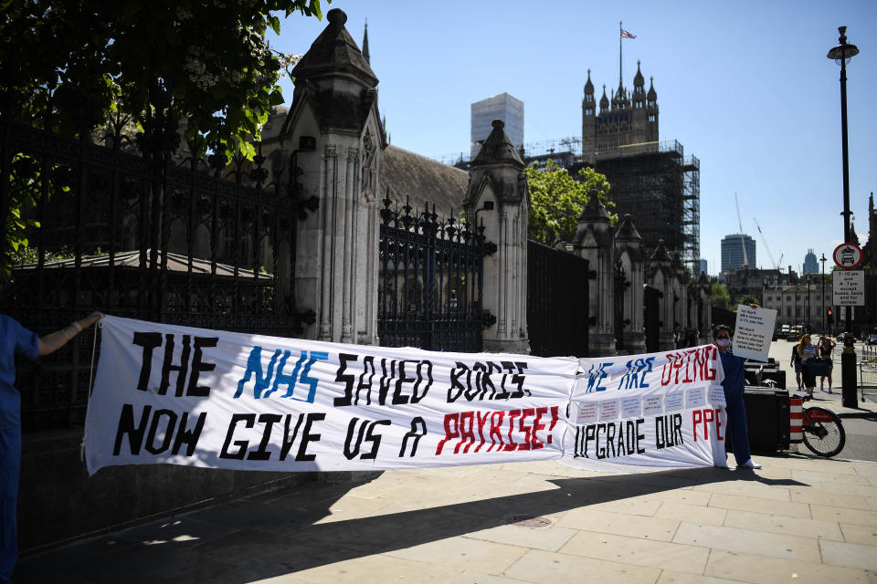 LONDON, ENGLAND - JUNE 25: NHS workers are seen holding a banner reading "The NHS saved Boris, now give us a pay rise" outside the Houses of Parliament on June 25, 2020 in London, England. British Prime Minister Boris Johnson was admitted to hospital in April after contracting Coronavirus. (Photo by Peter Summers/Getty Images)