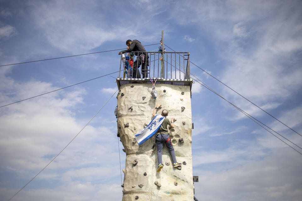 In this Friday, Feb. 21, 2020 photo, a boy with an Israeli flag attached to his neck climbs on a climbing wall during an event after the annual Jordan Valley parade in the West Bank Jordan Valley. Israel's Prime Minister Benjamin Netanyahu is eager to court the votes of the country's influential West Bank settlers in critical elections next month. President's Donald Trump's Mideast plan seemed to be the key to ramping up their support. The plan envisions Israel's eventual annexation of its scores of West Bank settlements — a long time settler dream. But in the weeks since it was unveiled, Netanyahu has stumbled over his promises to quickly carry out the annexation, sparking verbal attacks from settler leaders. (AP Photo/Ariel Schalit)