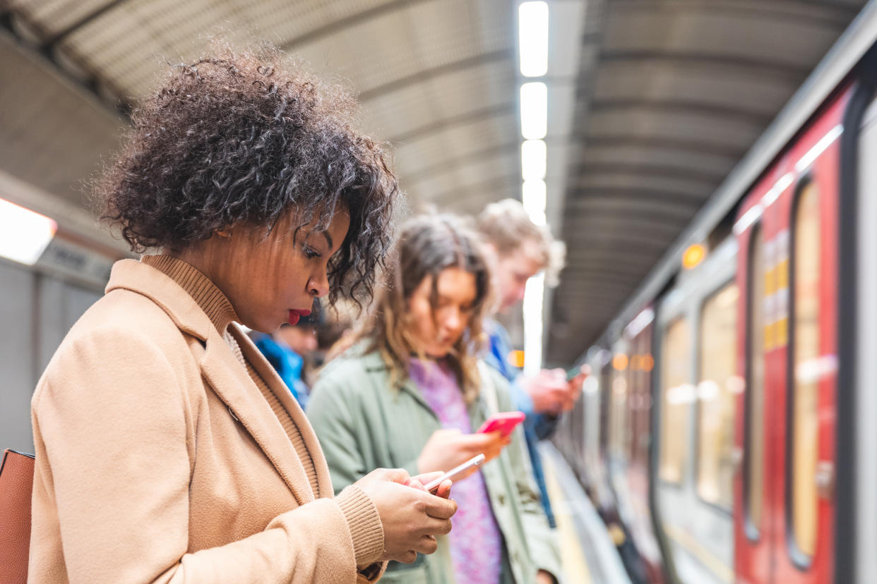 People using phones on tube platform. (Getty Images)