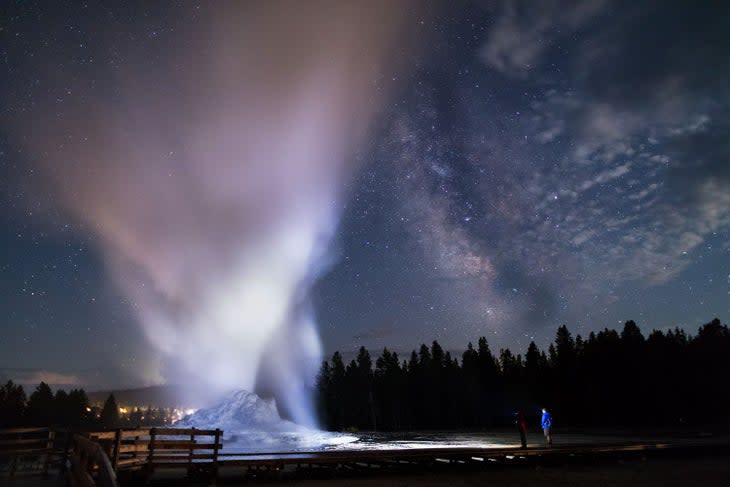 A father and son watch Castle Geyser erupt under the Milky Way in Yellowstone