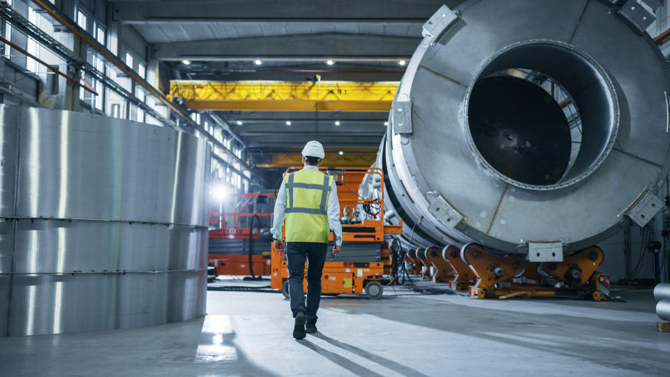 inflation Following Shot of Heavy Industry Engineers Walking Through Manufacturing Factory. In the Background Professionals Working on Construction of Oil, Gas and Fuel Pipeline Transportation Products