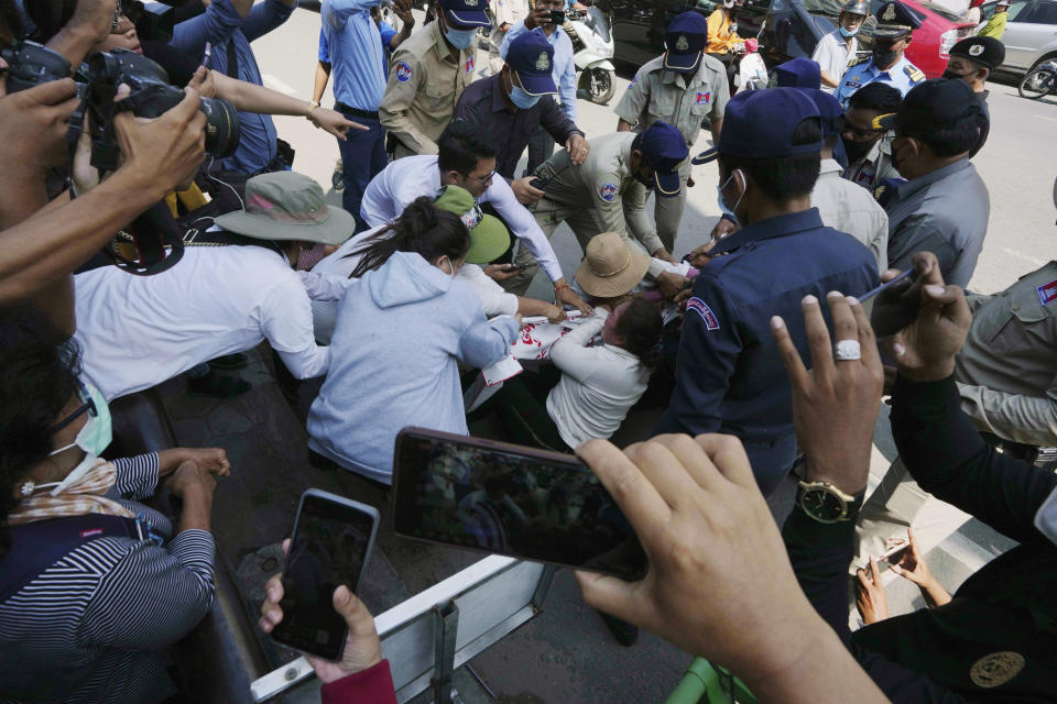 Local security personnel try to grab a banner from supporters of the Cambodia National Rescue Party in front of the the Phnom Penh Municipal Court in Phnom Penh, Cambodia, Tuesday, June 14, 2022. A Cambodian American lawyer and dozens of members of the now-dissolved opposition party were convicted of treason Tuesday in a trial that was the latest move to tame all opposition to the long-running rule of Prime Minister Hun Sen. (AP Photo/Heng Sinith)