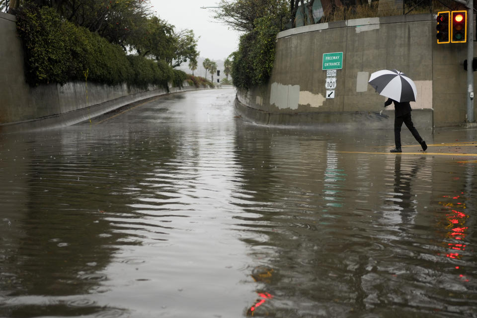 A pedestrian crosses an intersection near a freeway entrance during a rainstorm, Thursday, Dec. 21, 2023, in Santa Barbara, Calif. (AP Photo/Jae C. Hong)