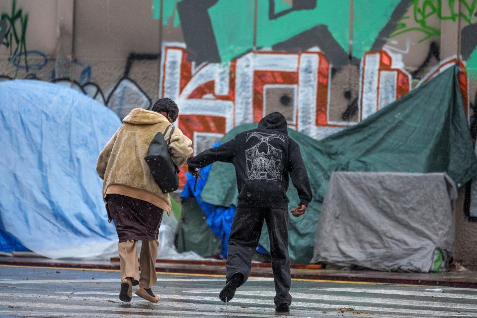 People cross the street under heavy rain in the Skid Row area, one of the largest populations of homeless people in the United States, Monday, Feb. 5, 2024, in Los Angeles.
