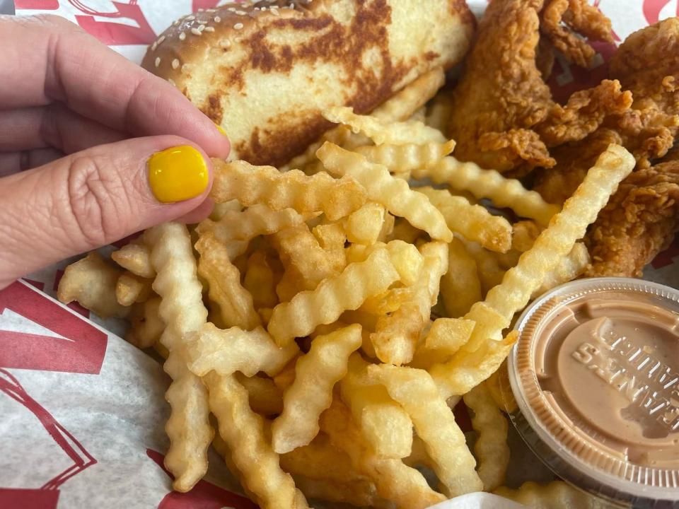 The writer holds a crinkle-cut fry above meal at Raising Cane's