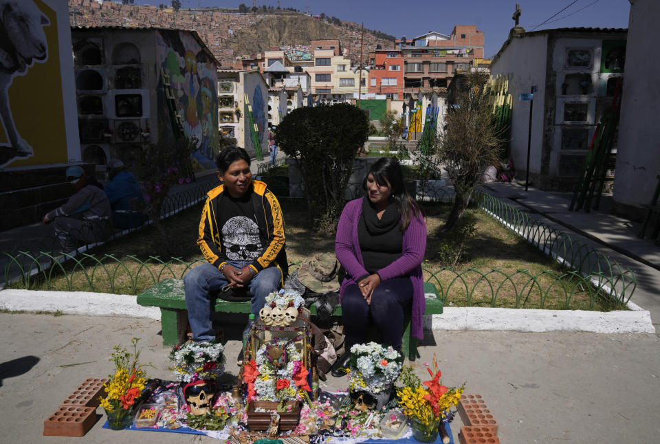 Una pareja se sienta con cráneos humanos decorados para ser bendecidos por un sacerdote en el Cementerio General durante la fiesta anual de las ñatitas, una tradición que marca el final de la festividad católica de Todos los Santos en La Paz, Bolivia, el martes 8 de noviembre de 2022. (AP Foto/Juan Karita)