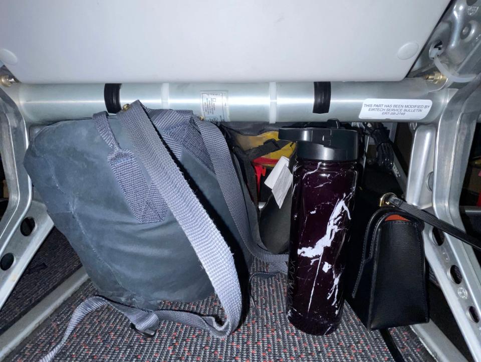 A backpack, purse, and water bottle beneath a seat Asia London Palomba PLAY Airlines