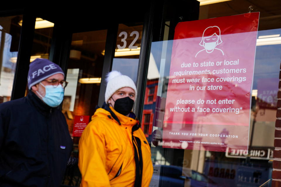 People wearing protective face masks walk past a business displaying a sign requiring face coverings.