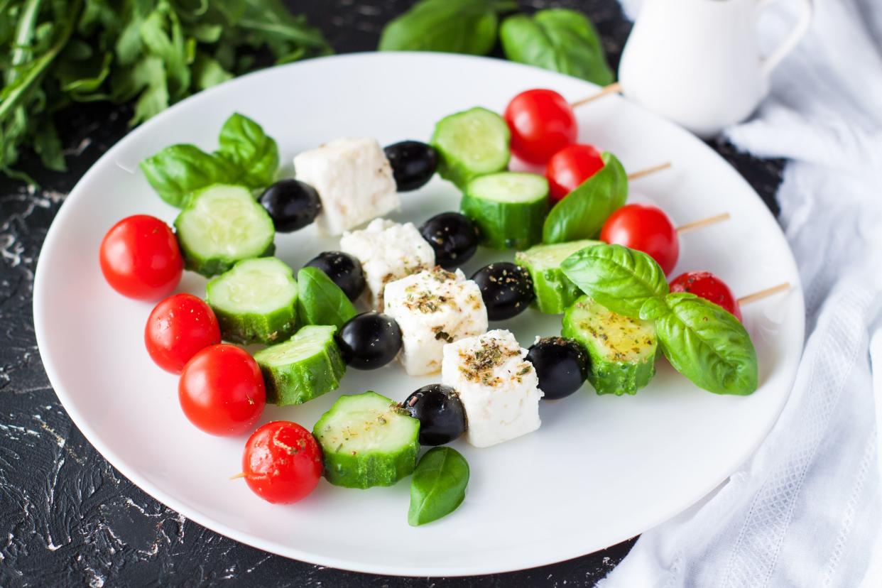 Fresh Greek salad skewers with feta, tomatoes, cucumbers, and olives served on white round plate