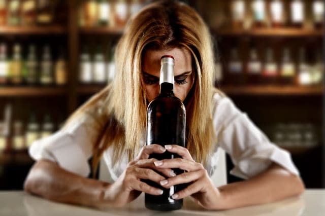 drunk alcoholic woman alone depressed with wine bottle in bar