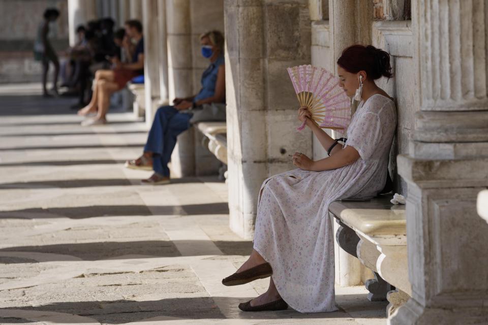 Tourists relax in the shade in St. Mark's square, in Venice, Italy, Thursday, June 17, 2021. After a 15-month pause in mass international travel, Venetians are contemplating how to welcome visitors back to the picture-postcard canals and Byzantine backdrops without suffering the indignities of crowds clogging its narrow alleyways, day-trippers perched on stoops to imbibe a panino and hordes of selfie-takers straining for a spot on the Rialto Bridge or in front of St. Mark’s Basilica. (AP Photo/Luca Bruno)