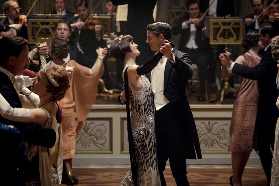 Michelle Dockery and Matthew Goode dressed in a silver gown and black suit dancing in a ballroom on the set of the new Downton Abbey movie