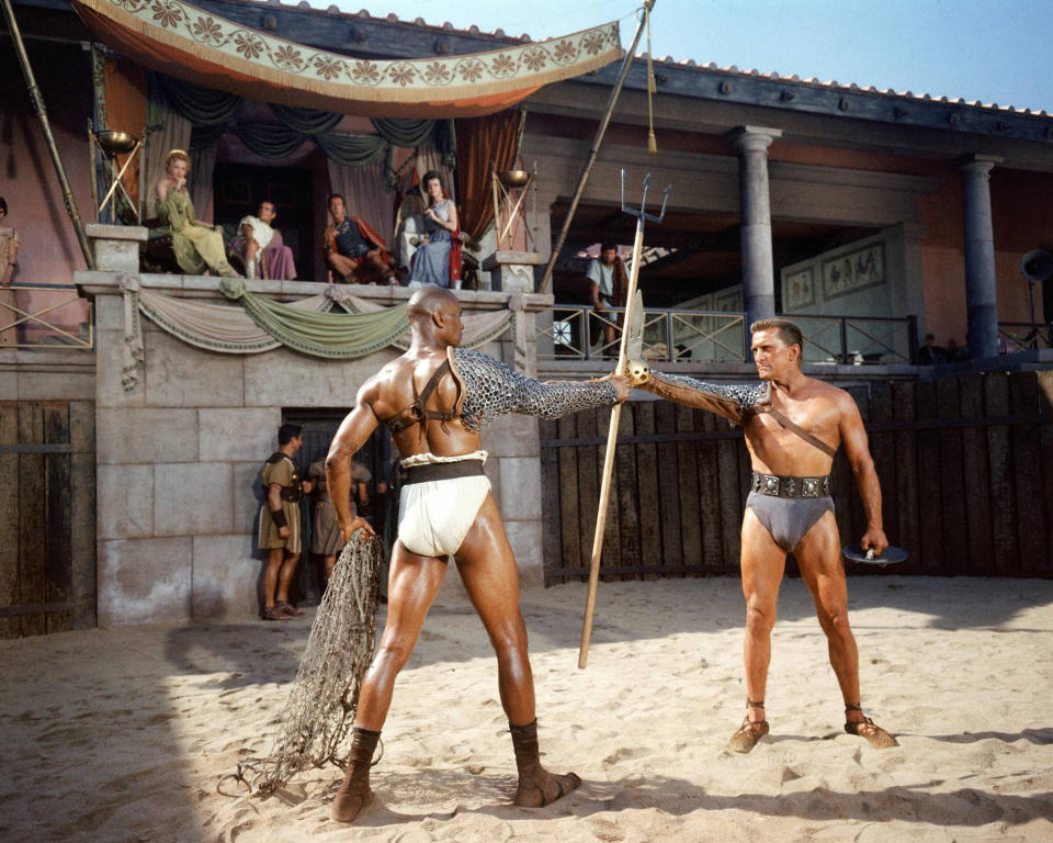 Woody Strode (1914-1994), US actor, Kirk Douglas, US actor, and in the background on the balcony, Laurence Olivier (1907-1989), British actor, John Gavin, US actor, and Nina Foch (1924-2008), Dutch actress, in a publicity still issued for the film, 'Spartacus', 1960. The historical drama, directed by Stanley Kubrick (1928-1999), starred Strode as 'Draba', Douglas as 'Spartacus', Olivier as 'Crassus', Gavin as 'Julius Caesar', and Foch as 'Helena Glabrus'. (Photo by Silver Screen Collection/Getty Images)