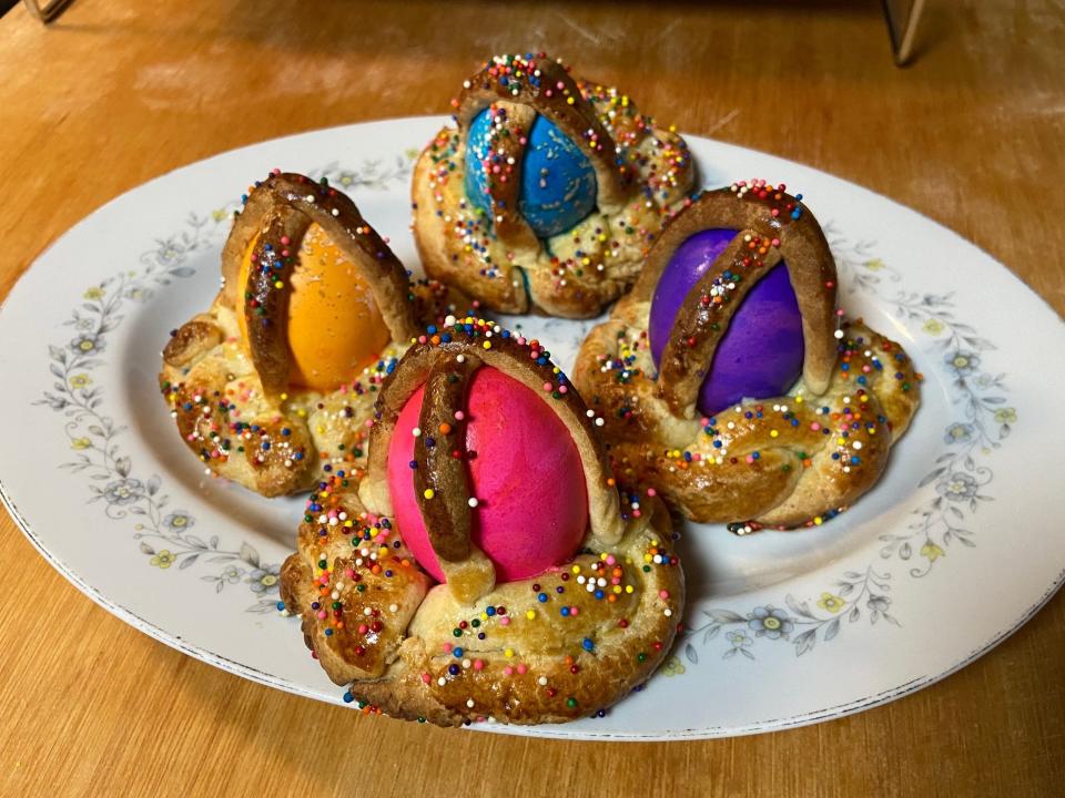 Four individual cooked breads with an orange, pink, blue, and purple egg in them on a plate.