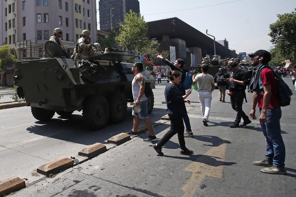 Demonstrators confront soldiers patrolling in an armored vehicle as a state of emergency remains in effect in Santiago, Chile, Sunday, Oct. 20, 2019. Protests in the country have spilled over into a new day, even after President Sebastian Pinera cancelled the subway fare hike that prompted massive and violent demonstrations. (AP Photo/Luis Hidalgo)