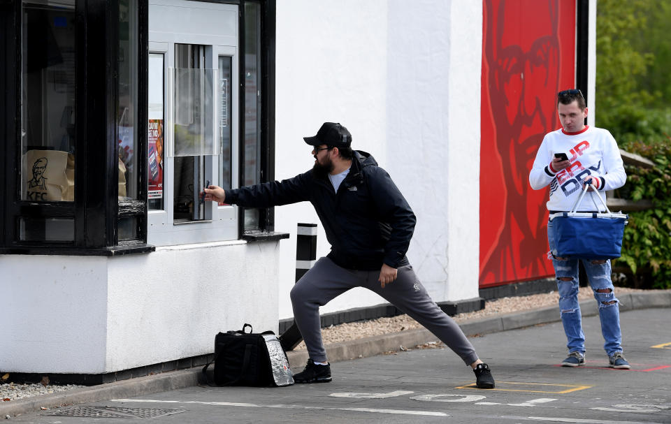 LEICESTER, ENGLAND  - MAY 02: A man tries to keep his distance while showing his phone to the staff as he picks up food from the KFC restaurant take-out booth on Narborough Road, Leicester on May 02, 2020 in Leicester, England. British Prime Minister Boris Johnson, who returned to Downing Street this week after recovering from Covid-19, said the country needed to continue its lockdown measures to avoid a second spike in infections. (Photo by Ross Kinnaird/Getty Images)