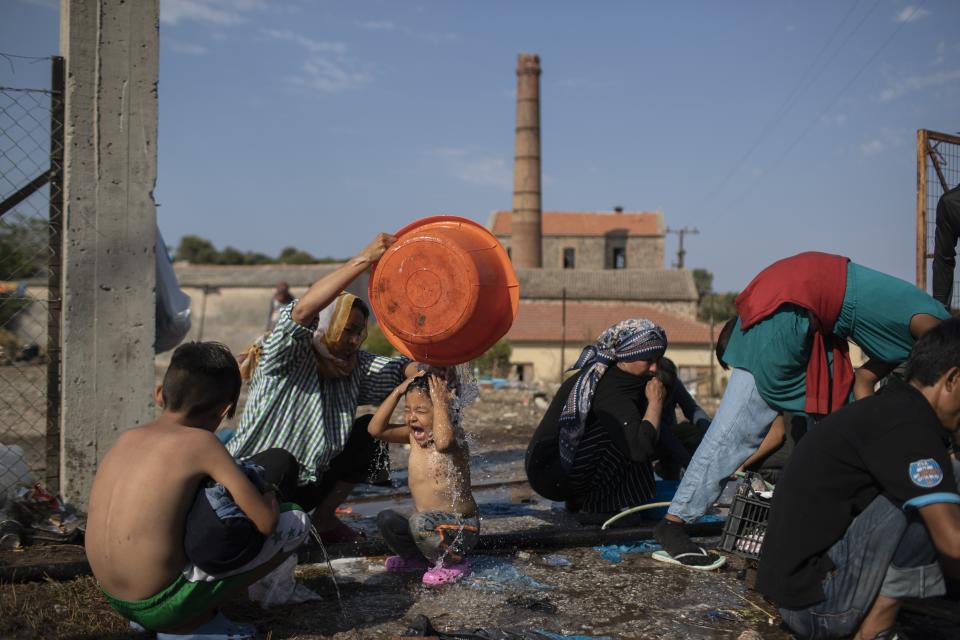 A woman washes a girl as migrants gather near Mytilene town, on the northeastern island of Lesbos, Greece, Saturday, Sept. 12, 2020. Greek authorities have been scrambling to find a way to house more than 12,000 people left in need of emergency shelter on the island after the fires deliberately set on Tuesday and Wednesday night gutted the Moria refugee camp. (AP Photo/Petros Giannakouris)