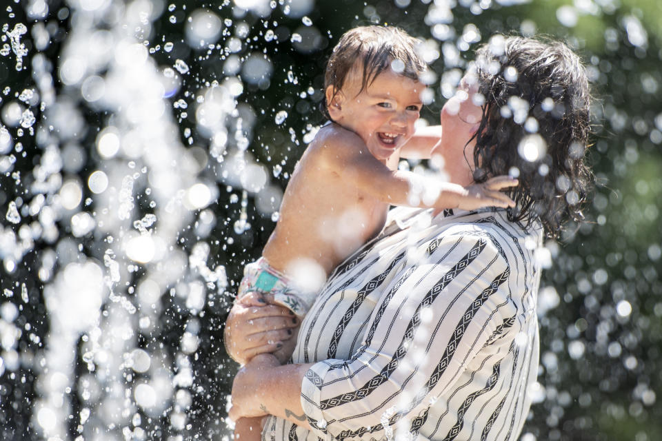 Jenny Rol, right, holds her 14-month-old daughter Safi in a water feature to cool off at a park in Missoula, Montana, as temperatures approached 100 degrees on Wednesday, June 30, 2021. A heat wave has gripped the Pacific Northwest and is moving east. (AP Photo/Tommy Martino)