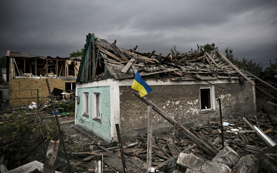 A Ukrainian flag is placed in front of a destroyed house after a strike in the city of Dobropillia - ARIS MESSINIS/AFP