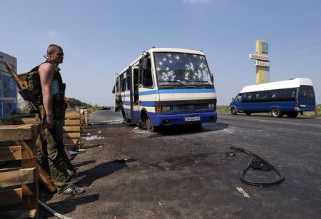 An armed pro-Russian separatist stands guard near a bus riddled with bullet holes at a checkpoint on the outskirts of Donetsk, August 13, 2014. REUTERS/Sergei Karpukhin