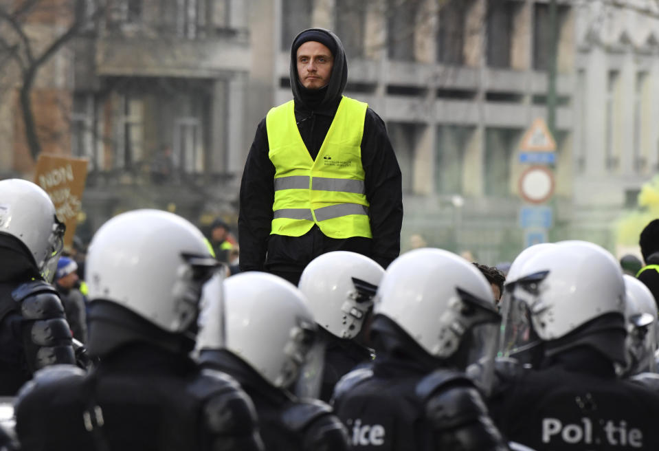 A protestor in a yellow vest stands above police during a demonstration in Brussels, Saturday, Dec. 8, 2018. Hundreds of police officers are being mobilized in Brussels Saturday, where yellow vest protesters last week clashed with police and torched two police vehicles. More than 70 people were detained. (AP Photo/Geert Vanden Wijngaert)