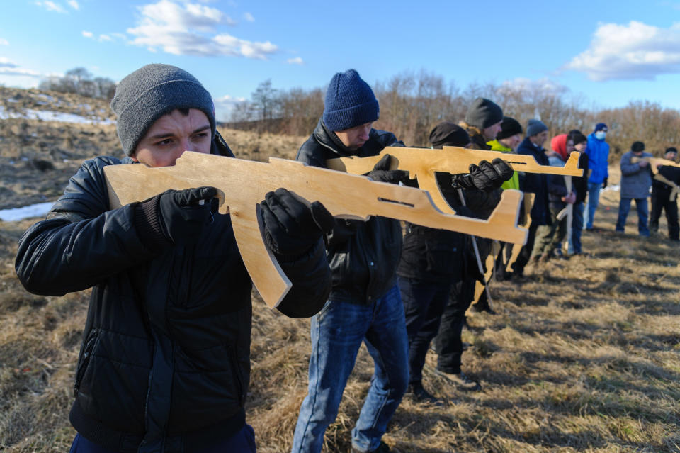 Ukrainians in civilian clothes take aim with wooden rifles during an open military training for civilians.