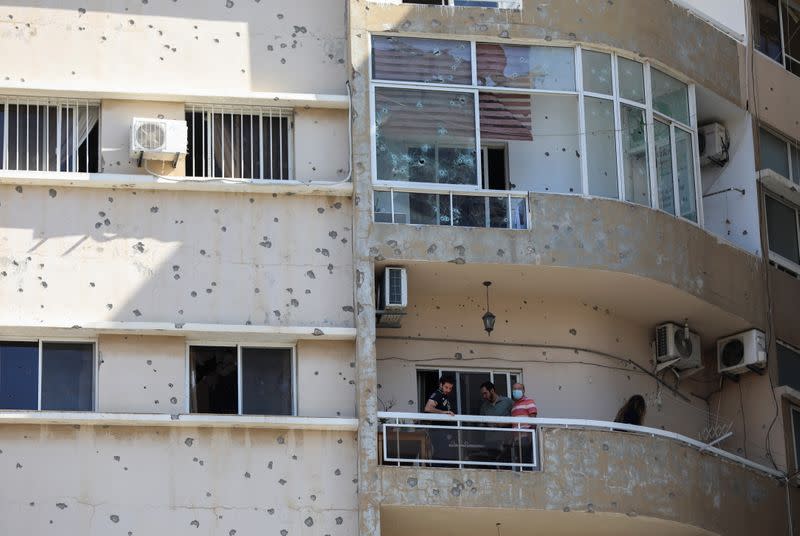 People stand on a balcony on a bullet-riddled building in Beirut