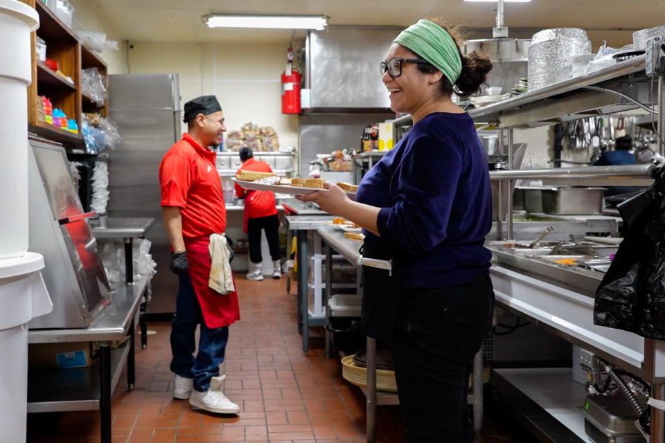 Waitress Diana Negrete laughs in the kitchen as she carries food to diners.