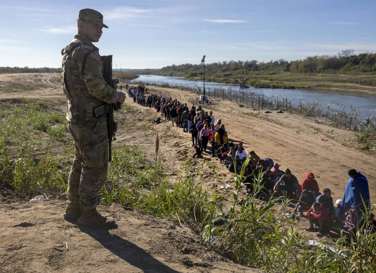 Un soldado de la Guardia Nacional de Texas vigila a un grupo de migrantes que cruzaron el Río Grande desde México en Eagle Pass, Texas, el 18 de diciembre de 2023. <a href="https://www.gettyimages.com/detail/news-photo/texas-national-guard-soldier-watches-over-a-group-of-more-news-photo/1865364688?adppopup=true" rel="nofollow noopener" target="_blank" data-ylk="slk:John Moore/Getty Images;elm:context_link;itc:0;sec:content-canvas" class="link ">John Moore/Getty Images</a>