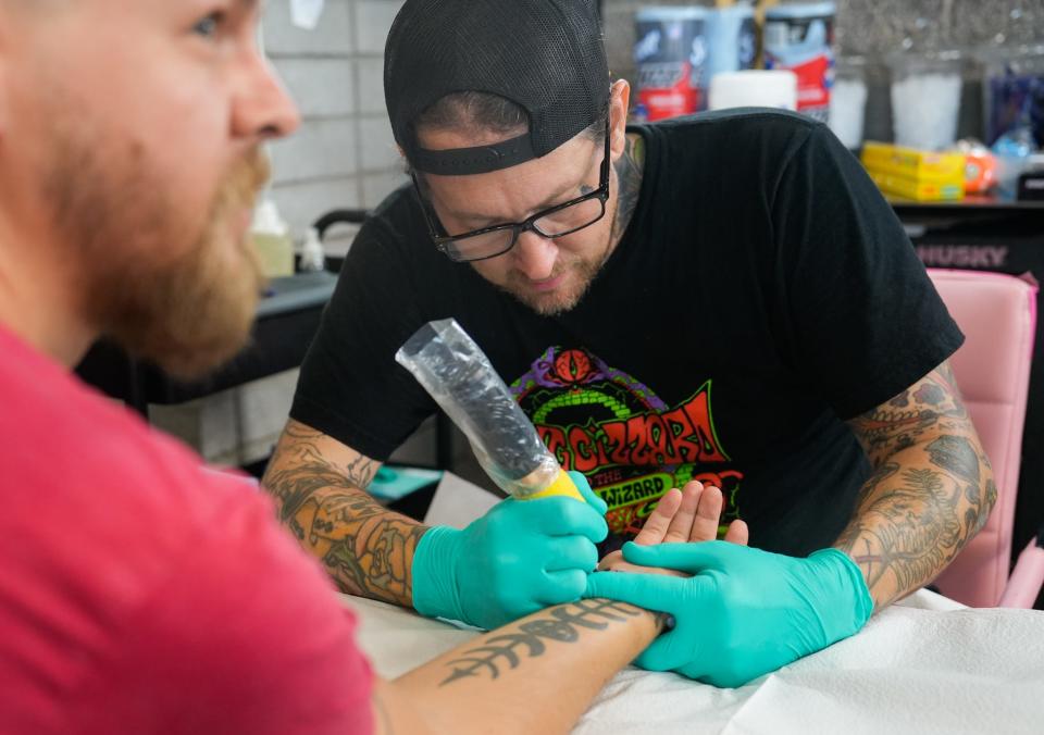 Tattoo artist Jason Anthony (back) tattoos the word "dissent" onto Aaron Quimby's wrist during a flash event for reproductive rights at the Golden Rule Tattoo on July 31, 2022, in Phoenix. All of the proceeds from the event will be donated to local charities that support reproductive rights.